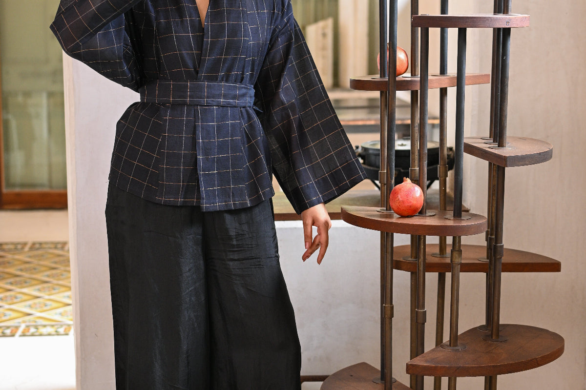 Woman in a checkered top and black pants standing next to a decorative wooden shelf.